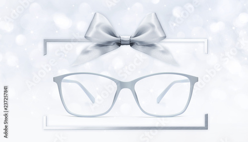 eyeglasses gift card, grey spectacles and silver ribbon bow in box frame isolated on blurred lights background