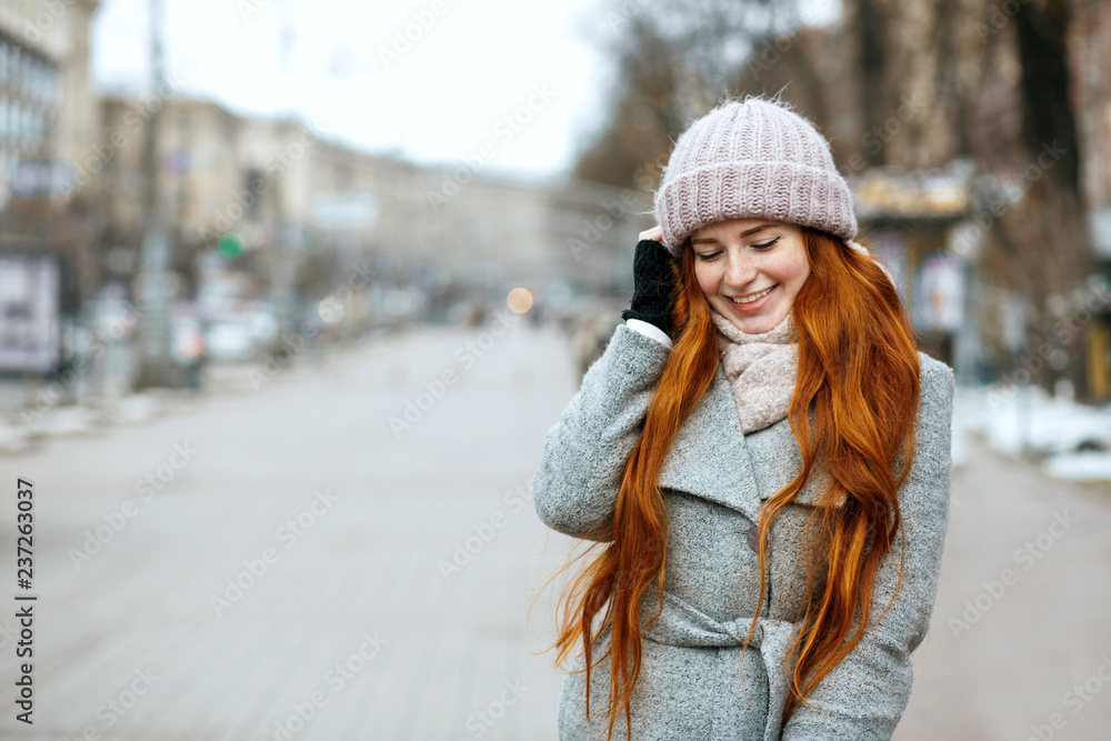 Urban portrait of happy ginger woman with long hair wearing warm clothes walking at the city. Empty space Urban portrait of happy ginger woman with long hair wearing warm clothes walking at the city. Empty space