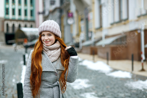 Charming red haired girl wearing warm winter clothes walking down the street. Empty space