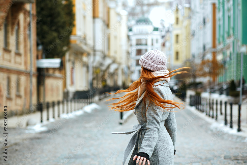 Awesome redhead lady wearing stylish winter outfit walking in city, spinning around. Empty space