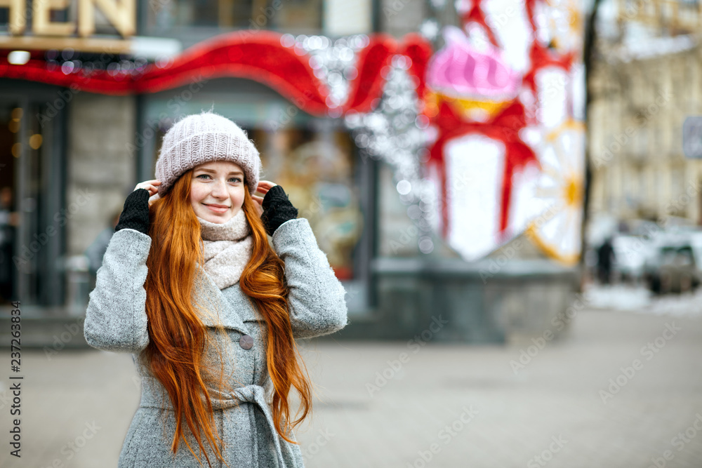 Urban portrait of joyful ginger model with long hair wearing warm clothes walking at the city. Empty space