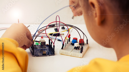 A cute girl constructs robot arduino and program it. The boards and microcontrollers are on the table. STEM education inscription. Programming. Mathematics. The science. Technologie. DIY.  photo