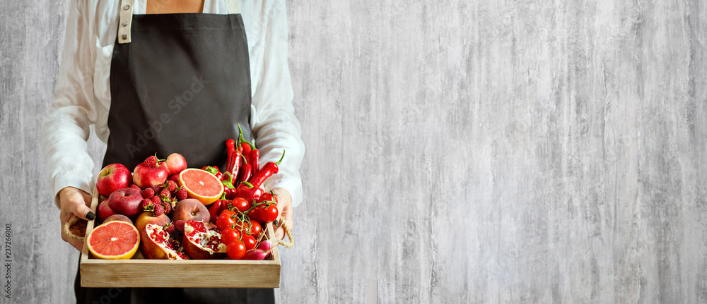 Fototapeta dziewczyna trzyma drewnianą tacę ze świeżych czerwonych warzyw i owoców na szarym tle. Zdrowe jedzenie koncepcja wegetariańska. Ścieśniać.