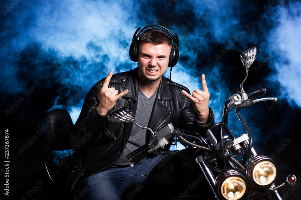 Cute biker in leather jacket is sitting on a motorcycle with headphones