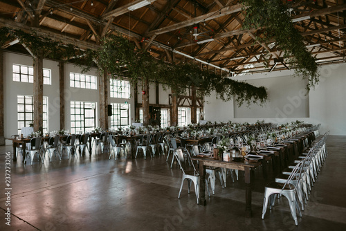 Long harvest tables with simple greenery and copper details in industrial setting for wedding photo