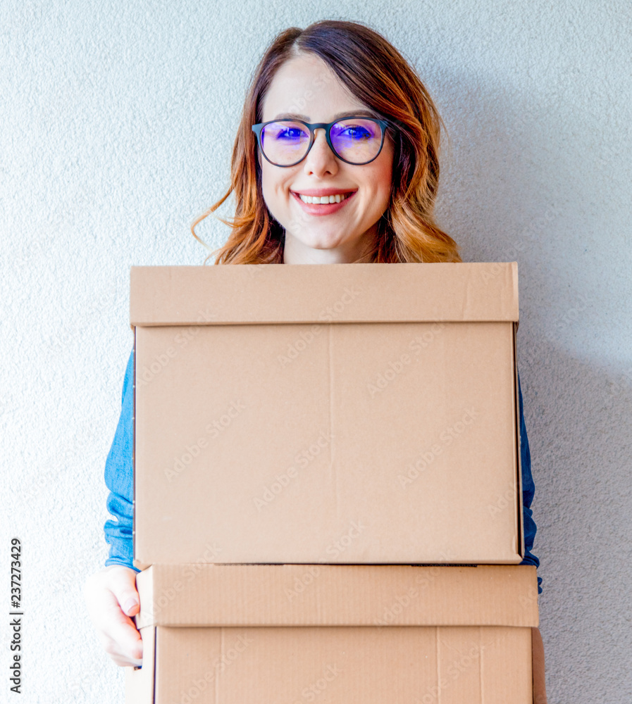 young redhead woman in jeans shirt standing on white wall with moving boxes. European ethnicity young redhead woman in jeans shirt standing on white wall with moving boxes. European ethnicity