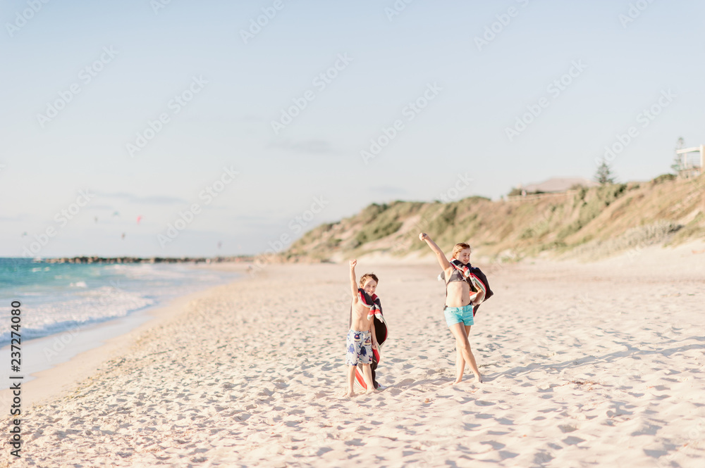 Two children at beach in victory poses with towel capes Two children at beach in victory poses with towel capes