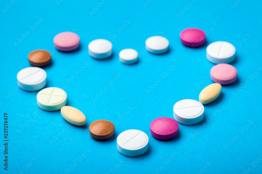 Heart laid out of pills on a blue background, drugs round and oval pills. Heart laid out of pills on a blue background, drugs round and oval pills.