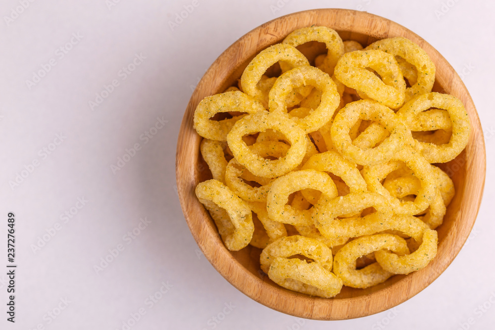 Puff corn rings in wooden bowl on light background
