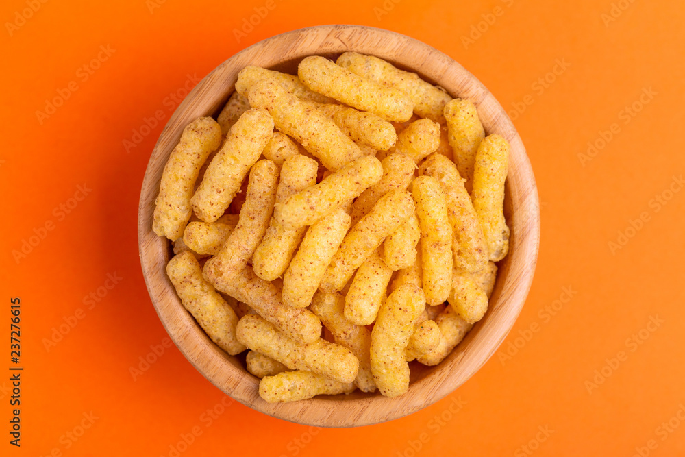 Crunchy corn sticks in wooden bowl on bright colored background Crunchy corn sticks in wooden bowl on bright colored background