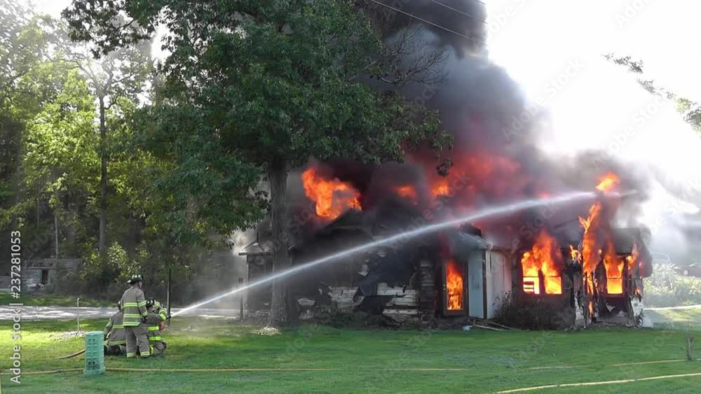 Firemen shooting a water hose towards a blazing house fire Firemen shooting a water hose towards a blazing house fire