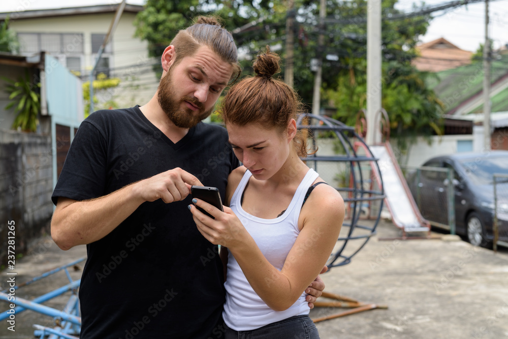Young couple using mobile phone together in the old playground Young couple using mobile phone together in the old playground