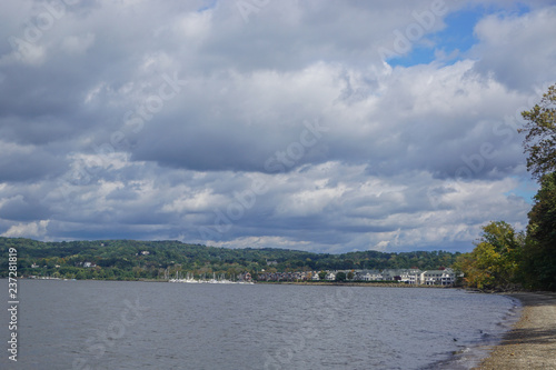Croton-On-Hudson, New York, USA: View of houses and a marina on the Hudson River under a cloud-filled sky, from a pebble beach in Croton Point Park.