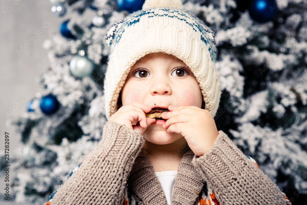 Christmas theme and children. Little Caucasian boy child in a warm hat and sweater posing, eating sweetness, dirty face. Christmas morning. New Year's holidays Christmas theme and children. Little Caucasian boy child in a warm hat and sweater posing, eating sweetness, dirty face. Christmas morning. New Year's holidays