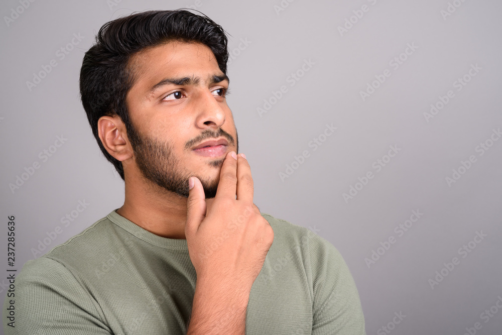 Portrait of young handsome Indian man thinking against gray background Portrait of young handsome Indian man thinking against gray background