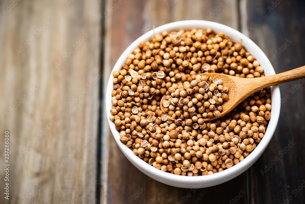 Dried coriander seeds in a bowl with wooden spoon on wooden table, herbs and spices, food ingredients Dried coriander seeds in a bowl with wooden spoon on wooden table, herbs and spices, food ingredients