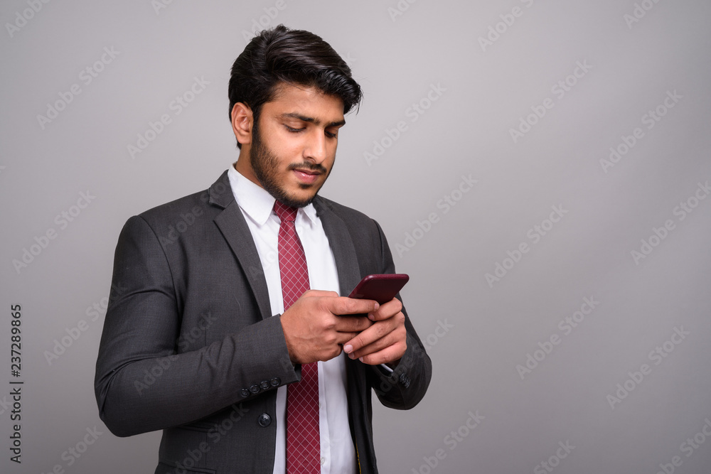 Portrait of Indian businessman using mobile phone against gray background Portrait of Indian businessman using mobile phone against gray background