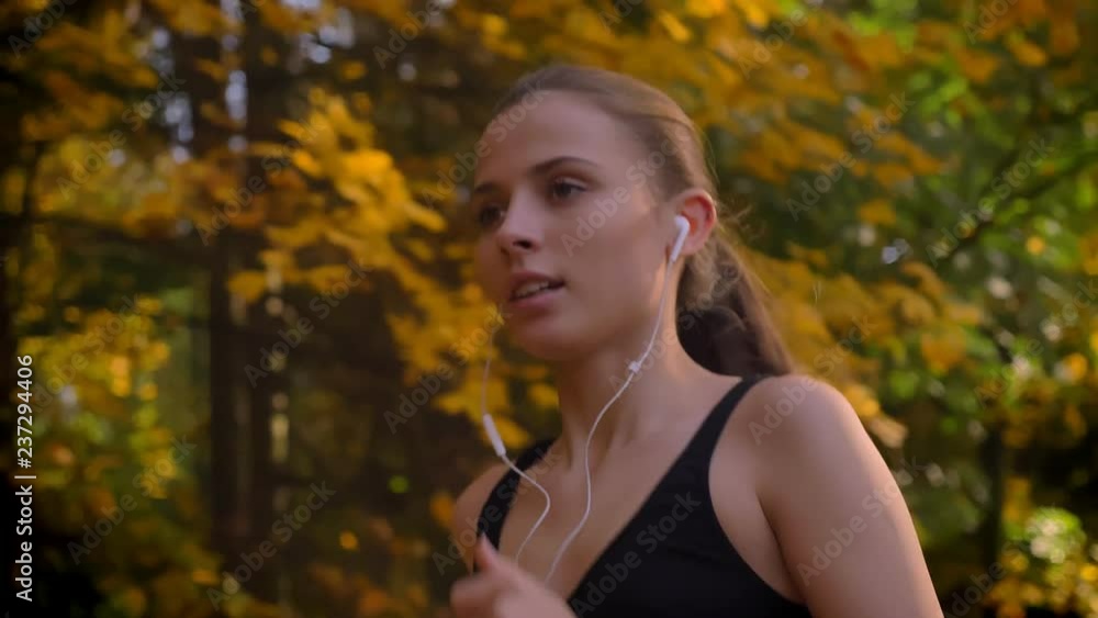 Dolly shot, close-up portrait of young attractive caucasian slim girl running in autumnal park with earphones. Dolly shot, close-up portrait of young attractive caucasian slim girl running in autumnal park with earphones.