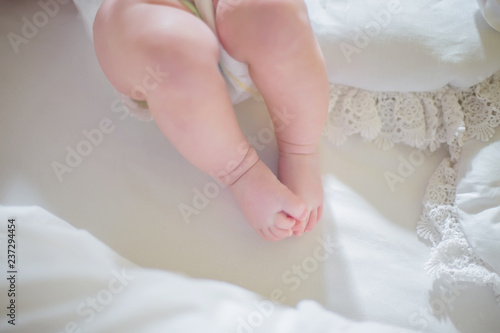 Legs of baby on the background of white sheets. The baby is lying in the crib among the pillows.