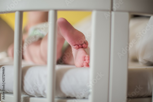 Legs of baby on the background of white sheets. The baby is lying in the crib among the pillows.