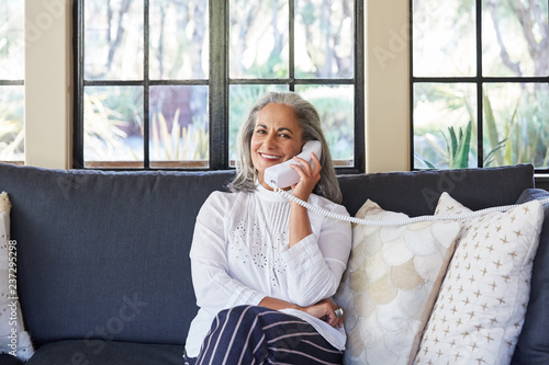 Portrait of mature woman with grey hair talking on landline phone in living room photo