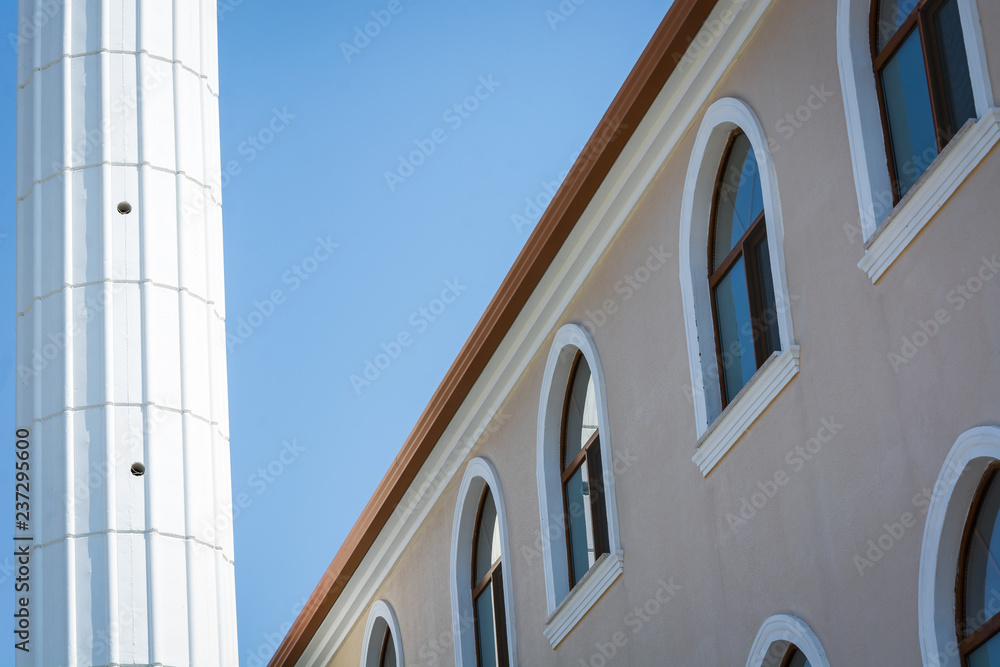High rise building with semicircular windows next to white column against blue sky. High rise building with semicircular windows next to white column against blue sky.