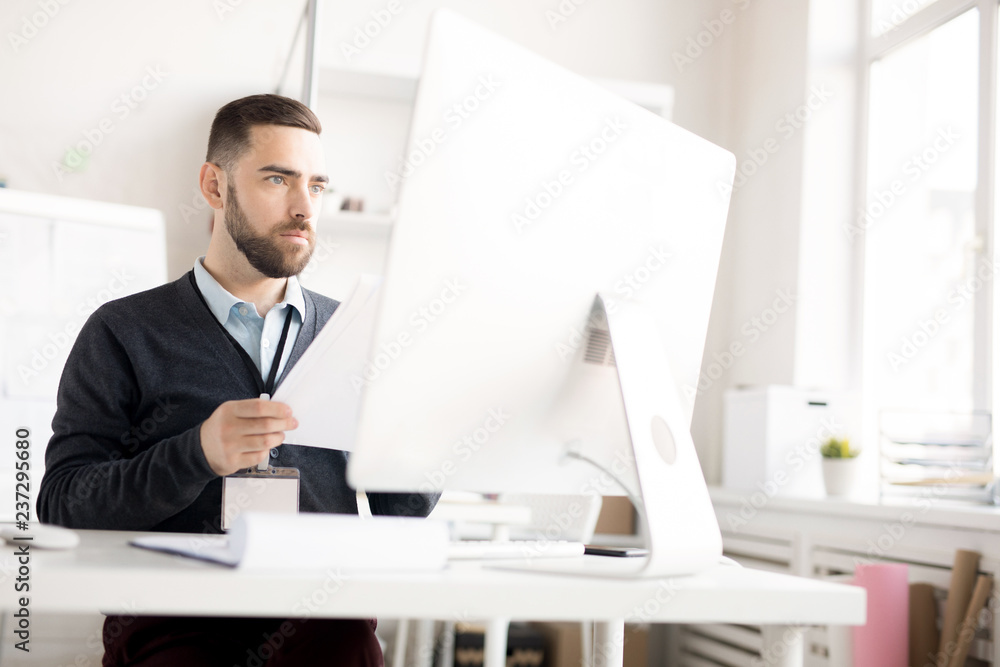 Portrait of handsome bearded businessman using computer while working at desk in modern office, copy space