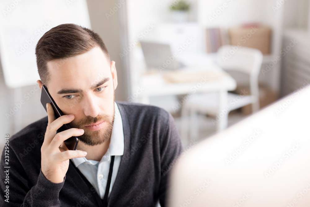 Head and shoulders portrait of handsome bearded businessman speaking by phone while working at desk in modern office, copy space Head and shoulders portrait of handsome bearded businessman speaking by phone while working at desk in modern office, copy space