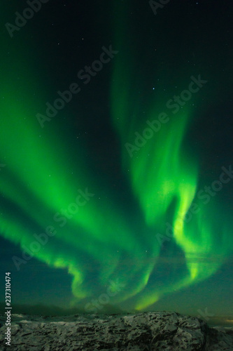 Beautiful stripes of the northern lights, aurora in the night sky above the snow covered hills. © Moroshka