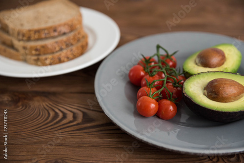 Preparing and cooking healthy avocado sandwich on dark rye toast bread made with fresh avocado paste, cherry tomatoes on brown wooden background