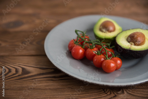 Healthy fresh avocado and cherry tomatoes on the plate on brown wooden background