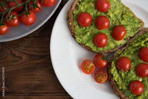 Healthy avocado sandwich on dark rye toast bread made with fresh avocado paste, cherry tomatoes on brown wooden background
