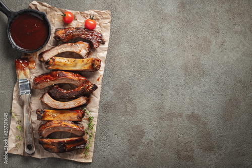 Closeup of pork ribs grilled with BBQ sauce and caramelized in honey. Tasty snack to beer on a paper for filing on dark concrete background. Top view with copy space. Flat lay