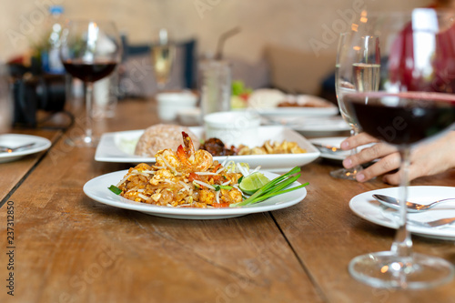 Famous Pad Thai noodles with shrimps and glass of red wine on wooden table.
