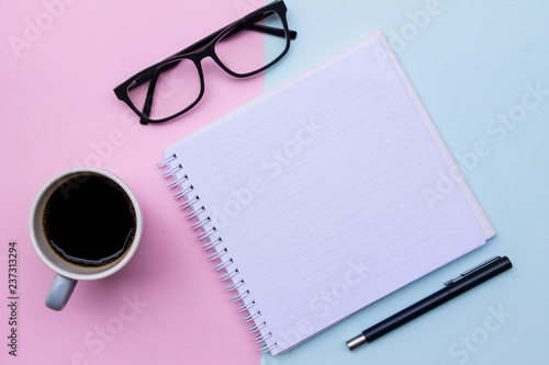 A cup of coffee, notebook, galsses and pen on blue and pink background