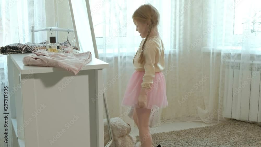 cheerful little girl with pigtails in a pink skirt tries on mother's shoes on heels and dances in front of a mirror with a bag, mother's wardrobe cheerful little girl with pigtails in a pink skirt tries on mother's shoes on heels and dances in front of a mirror with a bag, mother's wardrobe