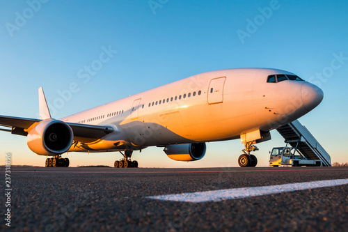 White wide-body passenger aircraft with air-stairs at the airport apron in the evening sun