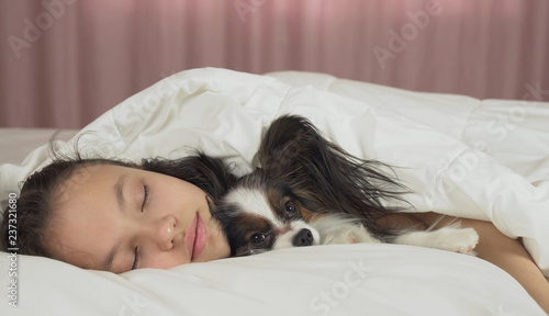Beautiful teen girl sleeping sweetly in bed with Papillon dog