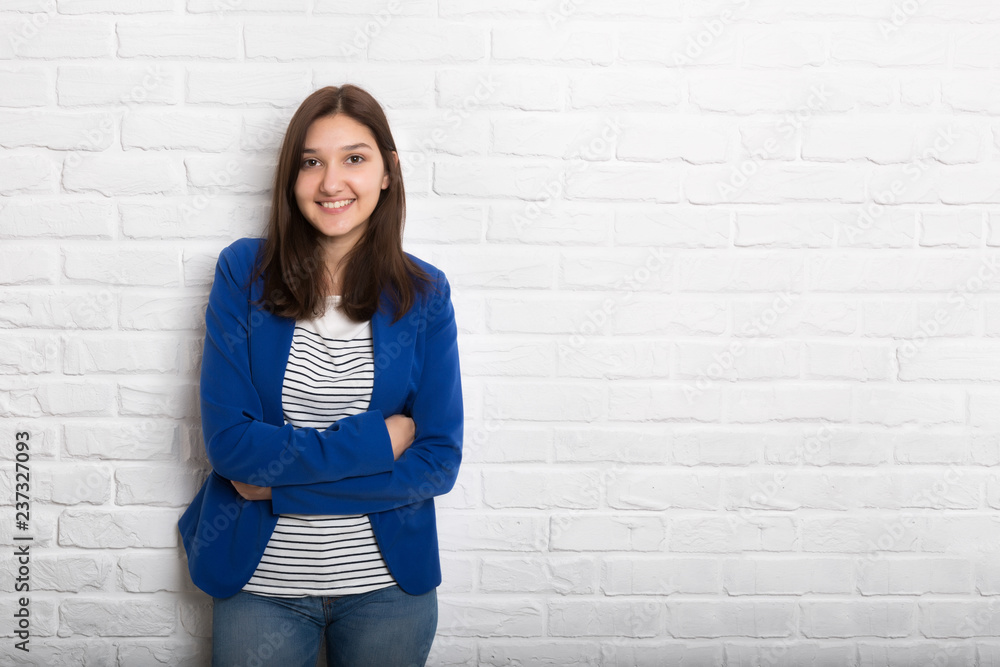 A young pretty smiling girl against a white loft-style brick wall. She looks at the viewer. Copy space. A young pretty smiling girl against a white loft-style brick wall. She looks at the viewer. Copy space.