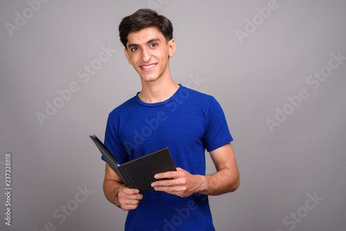 Young handsome Persian teenage boy student holding book