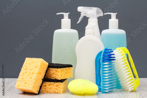 Obraz na plátne Bottles of dishwashing liquid, brushes and sponges on gray background