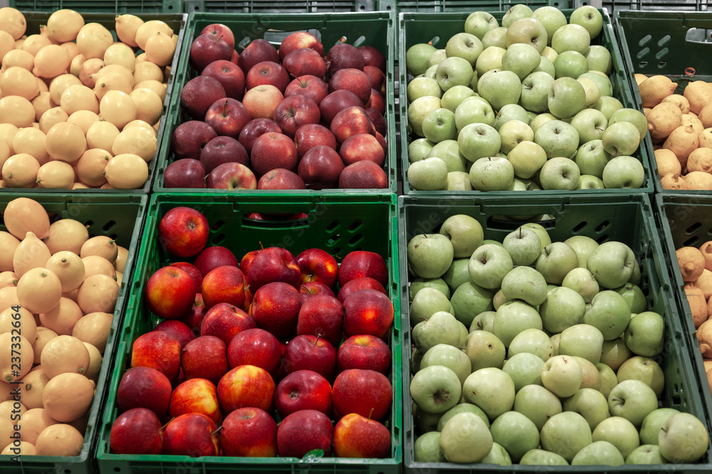 A large rack with baskets with different types of apples in the fruit department of the shopping center. Fresh and healthy foods for the diet on a daily basis among which bright red apples stand out