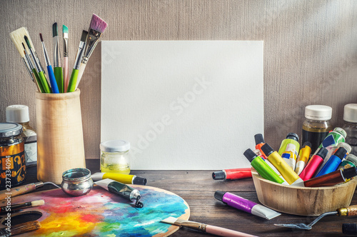 Painter equipment in a artist studio: empty canvas, tube of oil paint, art brushes, palette knife lying.  Artist workshop background. photo