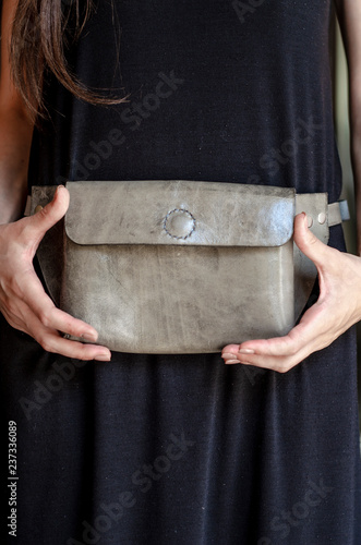 leather waist bag close- a leather little bag that hangs on the waist in a woman dressed in a black dress. Concept of bags, purses, leather goods for the advertisement of a store or a shop.