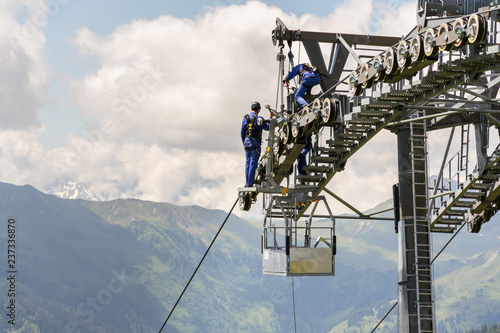 Two workers doing maintenance on cable car with Alps mountains in backgroun, Schonleitenbahn on Wildenkarkogel, Saalbach-Hinterglemm, Zell am See district, Salzburg federal state, Austria