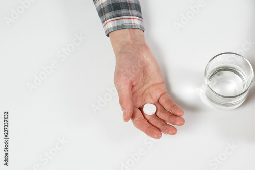 White pill and a glass of water in female hands.