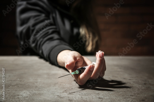 Female junkie with syringe at grey table. Concept of addiction
