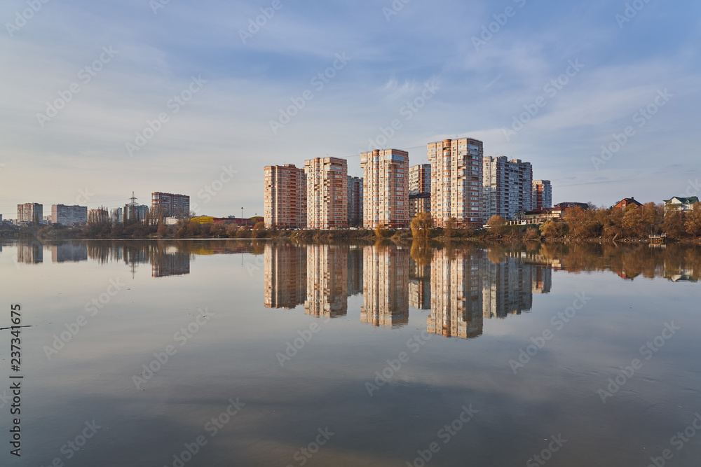 Panoramic View to the west of Krasnodar from the Kuban River in the winter at golden hours. New high-rise buildings and their reflection in the water surface. In the background is a clear blue sky.