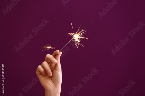Woman holding Christmas sparkler on color background