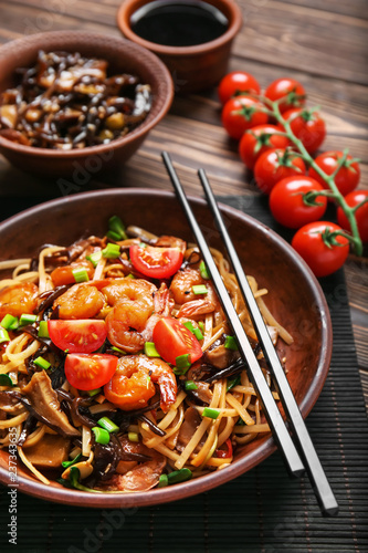 Plate with tasty chinese noodles, mushrooms and vegetables on wooden table, closeup